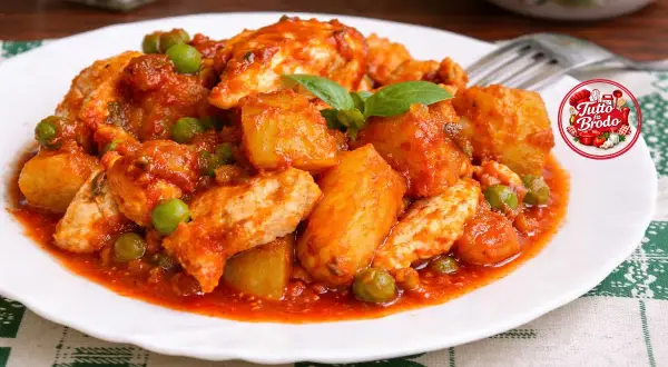 Un saporito spezzatino di pollo con patate e piselli in salsa rossa, guarnito con basilico fresco.