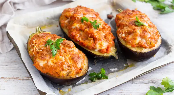 Melanzane ripiene al forno velocissime, dorate e filanti, guarnite con prezzemolo fresco su una teglia.