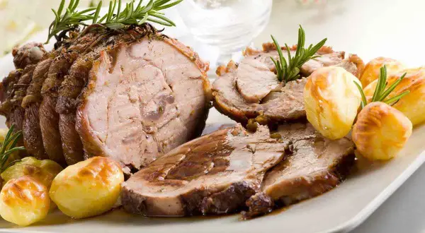 Succulento arrosto di vitello affettato, guarnito con rosmarino e accompagnato da patate arrosto dorate.