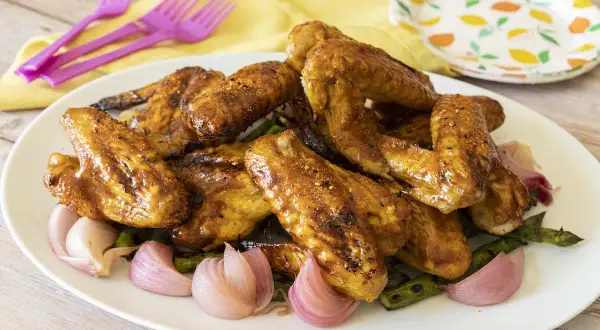 Alette di pollo dorate e succulente, servite con cipolle rosse e asparagi su un piatto bianco.