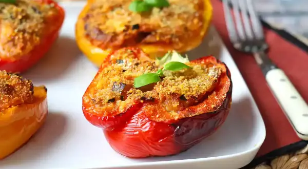 Peperoni ripieni al forno, colorati e invitanti, con un ripieno dorato e una fogliolina di basilico fresco.