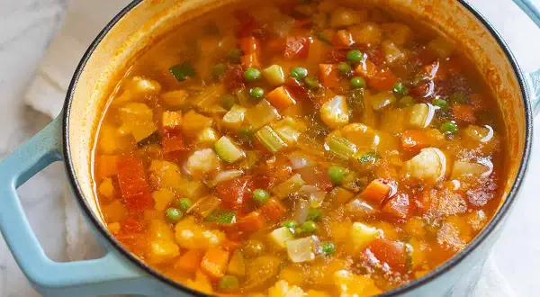 Un fumante minestrone di verdure in una casseruola azzurra, ricco di carote, zucchine, piselli e pomodoro.
