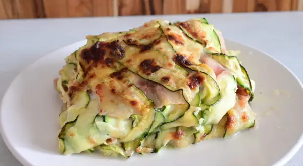 Una fetta di parmigiana di zucchine light, con strati di zucchine sottili, formaggio filante e prosciutto cotto, gratinata al forno.