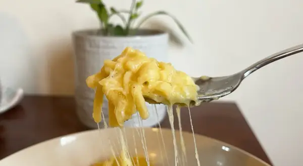 Un primo piatto cremoso: pasta e patate con provola filante, servita su una forchetta.