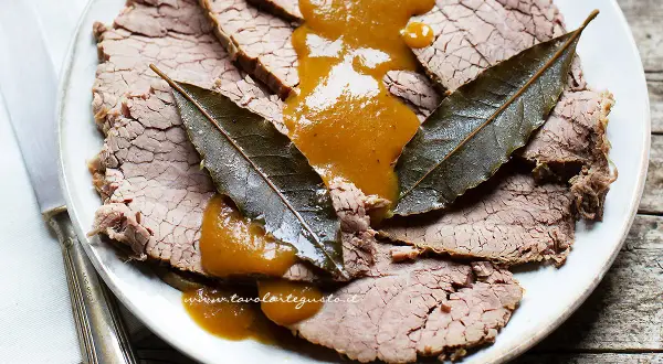 Fette di brasato di manzo succulento su un piatto, nappate con una salsa dorata e guarnite con foglie di alloro.