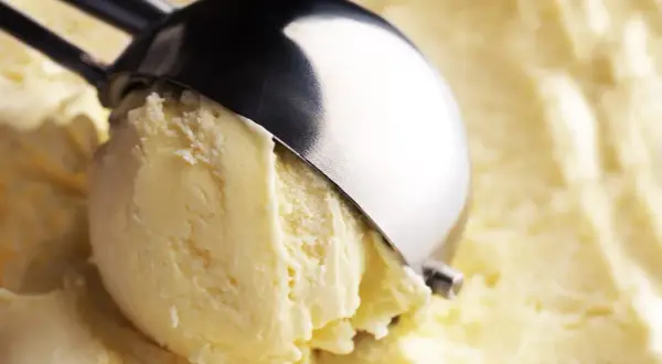 Un cucchiaio raccoglie una pallina di cremoso gelato fatto in casa, dal colore giallo pallido e dalla consistenza invitante.