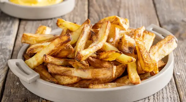 Patate in friggitrice ad aria, dorate e croccanti, servite in una ciotola su un tavolo di legno.