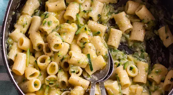 Close-up of rigatoni pasta with zucchini in a creamy sauce in a pot.