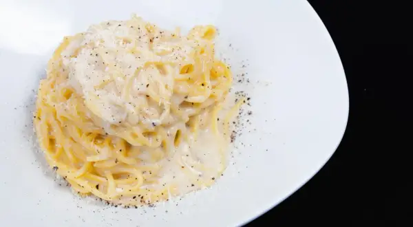 Spaghetti cremosi con formaggio e pepe nero, un classico della cacio e pepe ricetta, serviti su un piatto bianco.