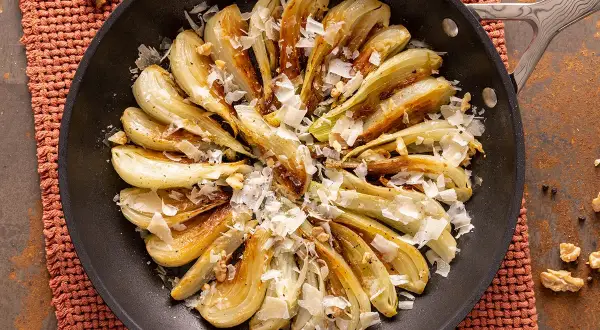 Finocchi in padella dorati, guarniti con scaglie di formaggio e noci croccanti. Un piatto semplice e gustoso.