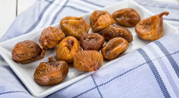 Fichi secchi al forno, caramellati e lucidi, disposti su un piatto bianco, con un tovagliolo a quadri blu e bianchi.