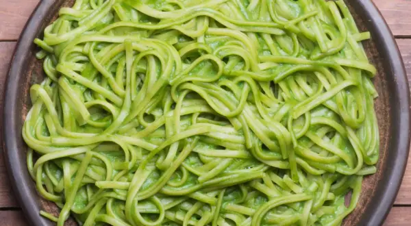 Pasta fresca condita con una cremosa salsa verde, probabilmente crema di zucchine per pasta, servita in un piatto scuro.