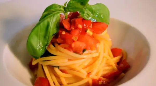 Spaghetti conditi con un fresco sugo con pomodorini freschi e basilico, un piatto semplice e gustoso.