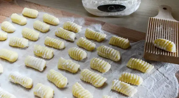 Gnocchi di patate ricetta: tanti piccoli gnocchi fatti in casa, pronti per essere cotti. Sullo sfondo, farina e un attrezzo per rigarli.