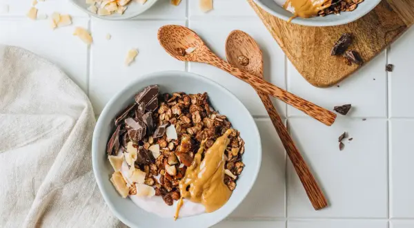 Una ciotola di granola fatta in casa con yogurt, burro di arachidi, scaglie di cocco e pezzi di cioccolato fondente.