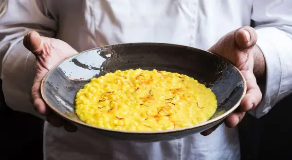 Chef presenta un cremoso risotto alla milanese, dorato e profumato, guarnito con fili di zafferano.