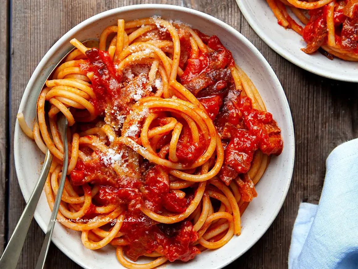 Un piatto invitante di bucatini all'amatriciana ricetta, conditi con sugo rosso e guanciale croccante, spolverati di pecorino.