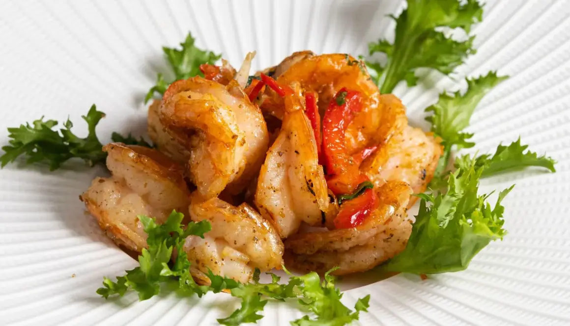 Gamberi sale e pepe succulenti, saltati con pomodorini e guarniti con insalata fresca su un piatto bianco texturizzato.