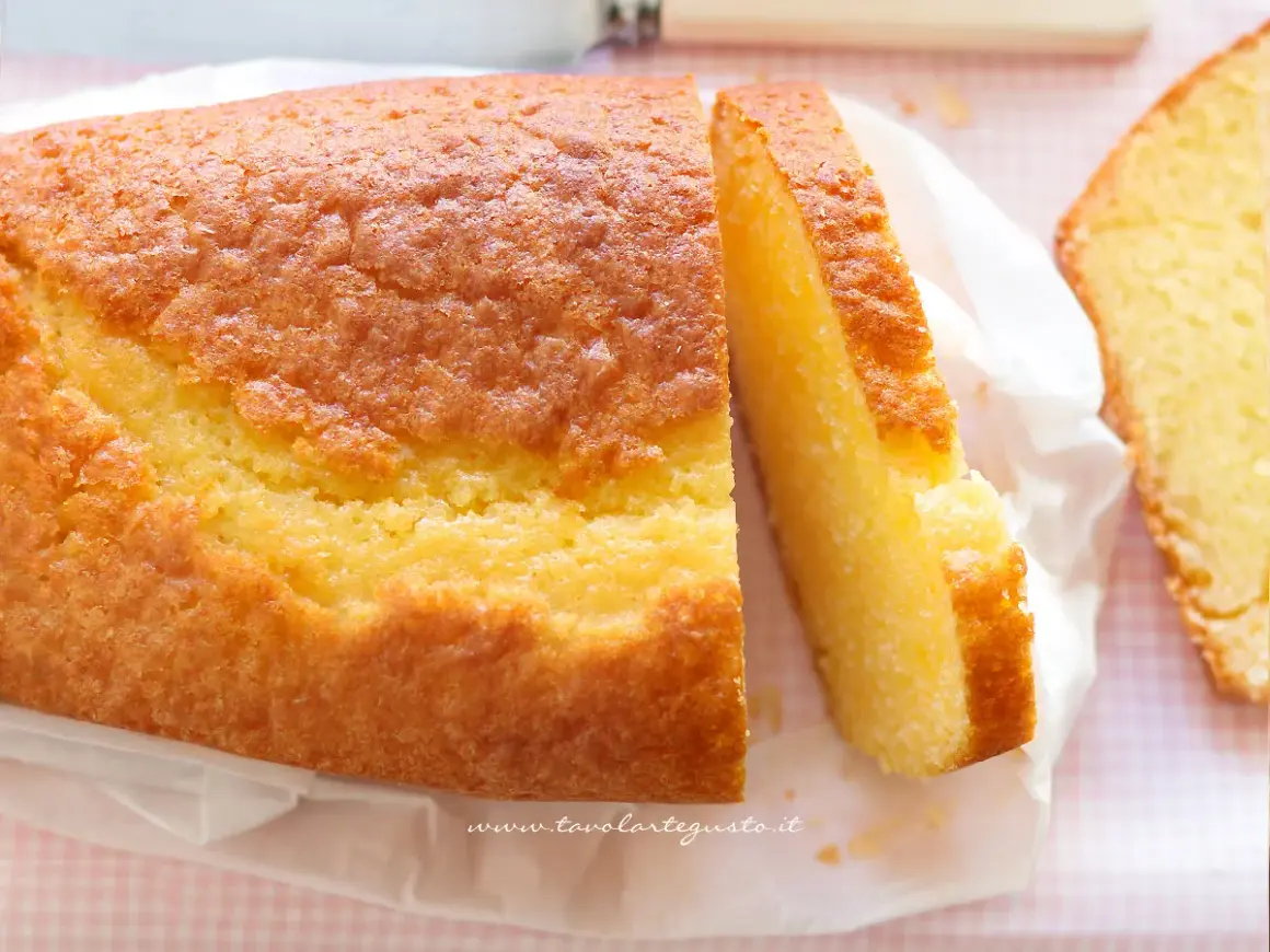 Un soffice plumcake allo yogurt, dorato e invitante, con una fetta tagliata che ne mostra la morbidezza. Perfetto per la colazione.