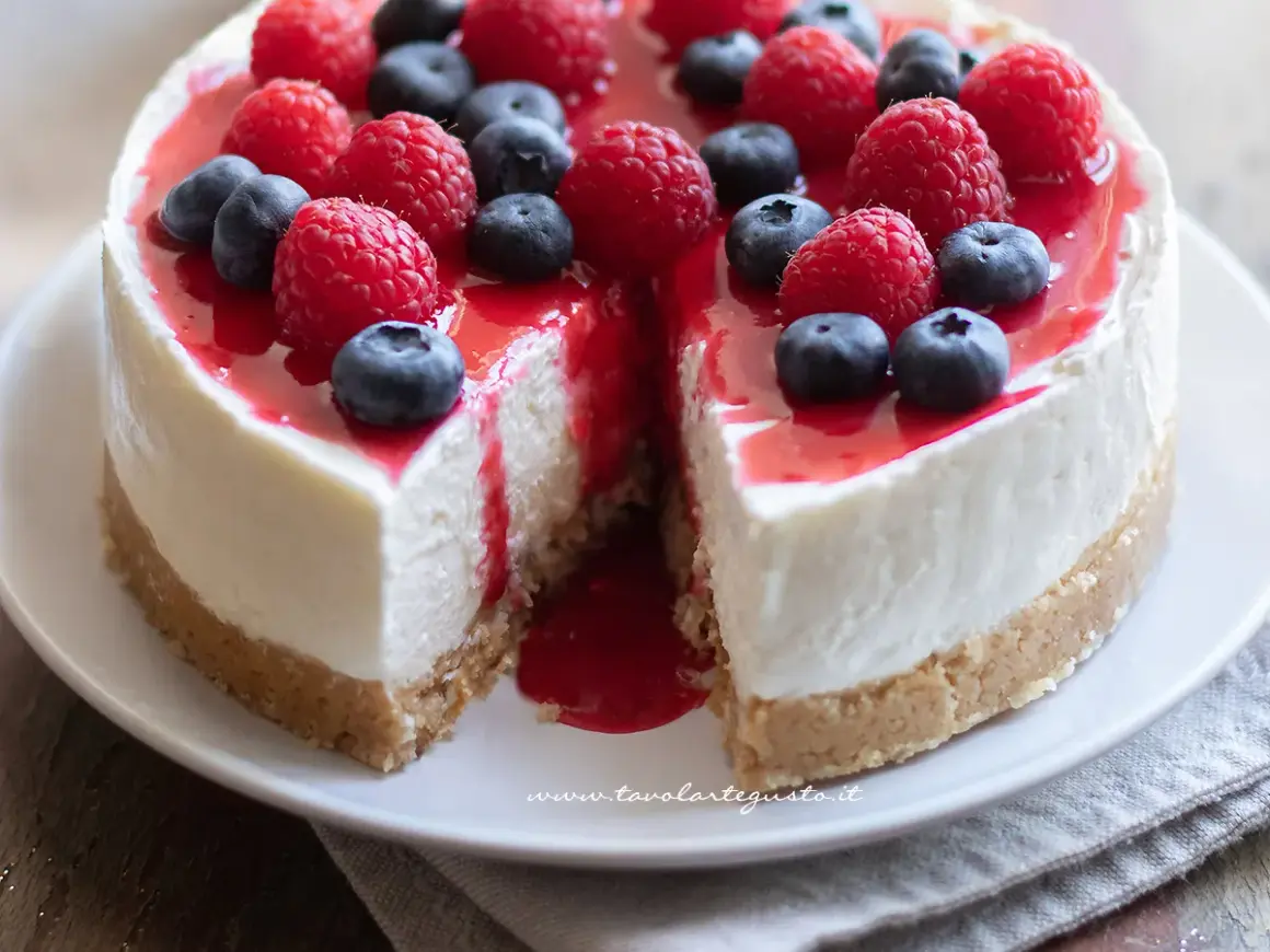 Cheesecake con mascarpone, guarnita con lamponi e mirtilli freschi, con una colata di salsa rossa.