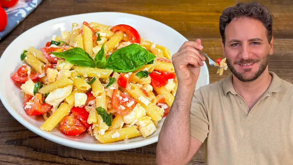 Un uomo sorride mentre assaggia una forchettata di pasta alla crudaiola, un piatto fresco con pomodorini, mozzarella e basilico.