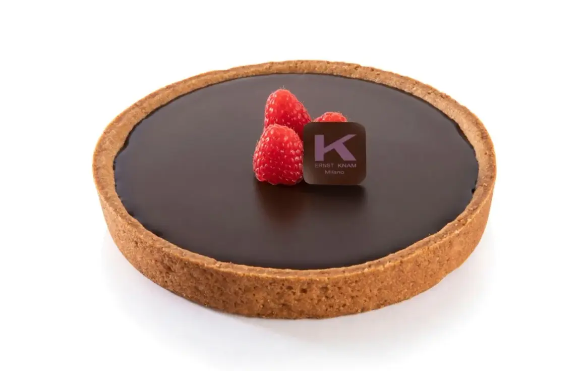 Una deliziosa crostata al cioccolato, con tre lamponi freschi e il logo di Ernst Knam.