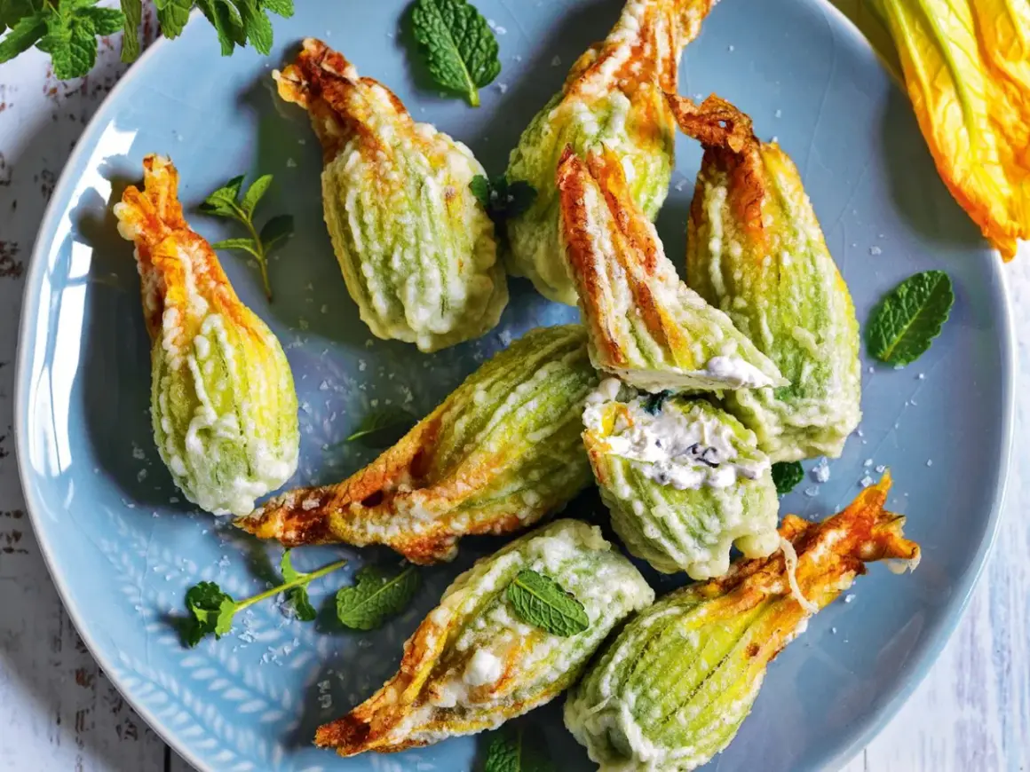 Fiori di zucca fritti, ripieni di formaggio cremoso e guarniti con menta fresca, su un piatto blu.