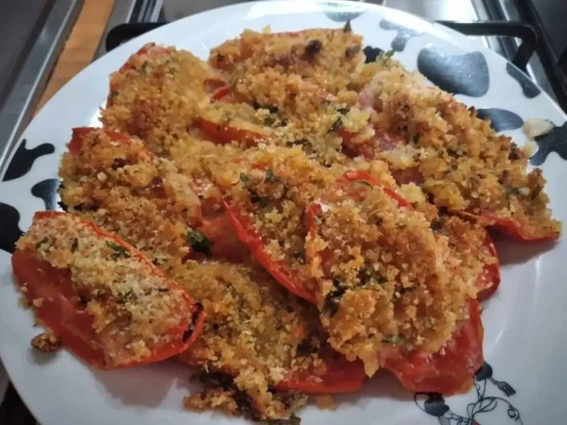 Pomodori al forno ripieni di pangrattato e erbe aromatiche, dorati e invitanti.