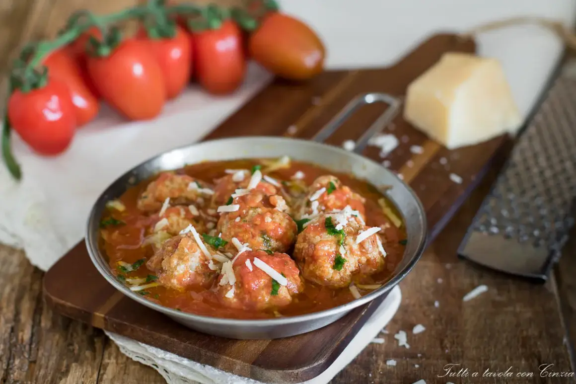 Polpette al sugo ricetta della nonna, succulente e profumate, servite in un piatto di metallo con pomodori freschi e parmigiano.