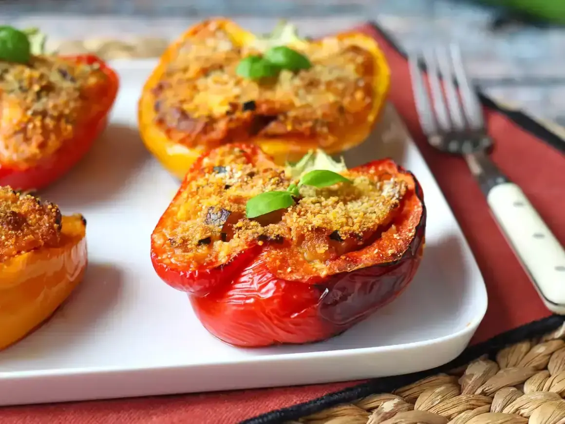Peperoni ripieni al forno, colorati e invitanti, con un ripieno dorato e una fogliolina di basilico fresco.