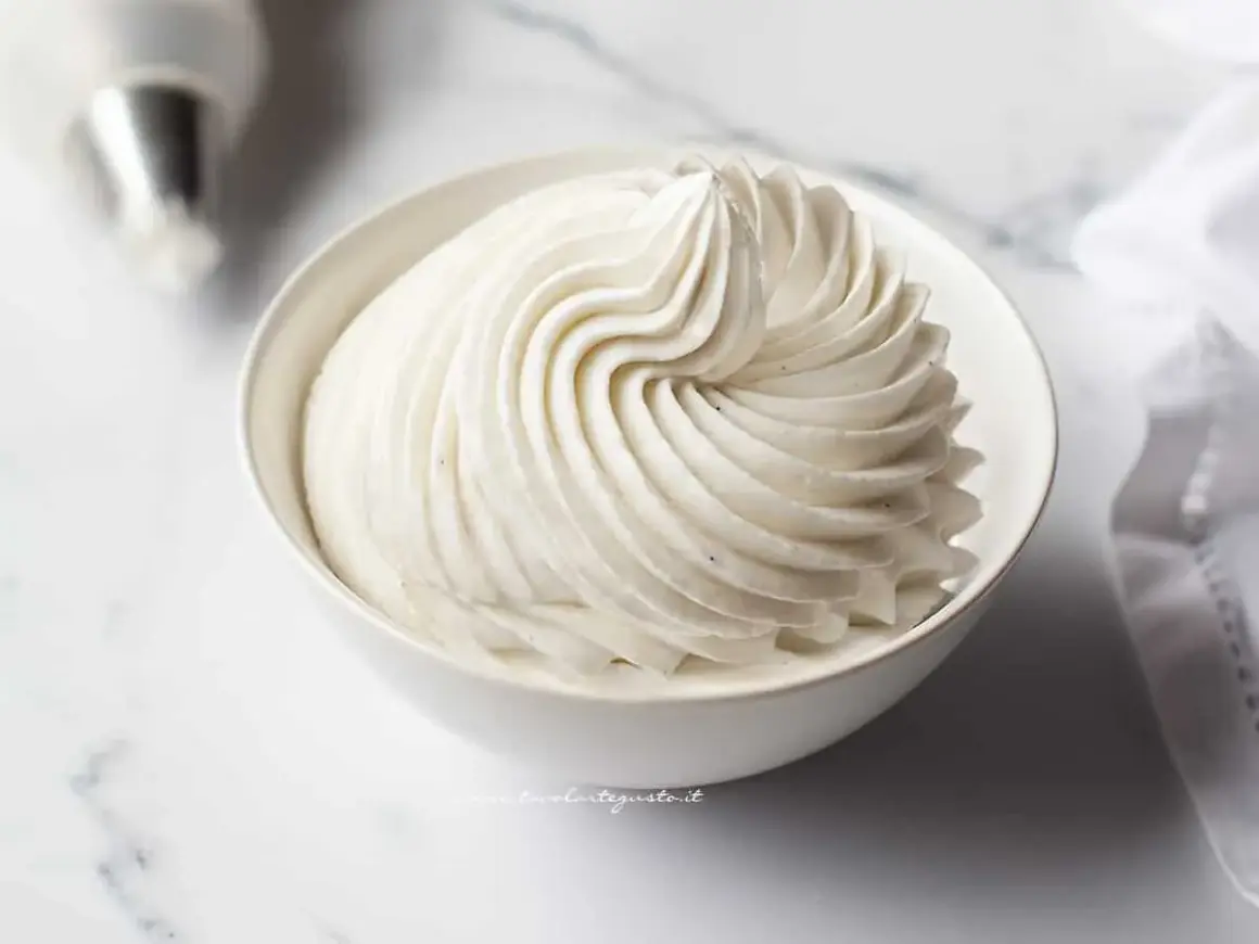 Una ciotola bianca piena di soffice crema chantilly, con striature perfette e puntini di vaniglia visibili.
