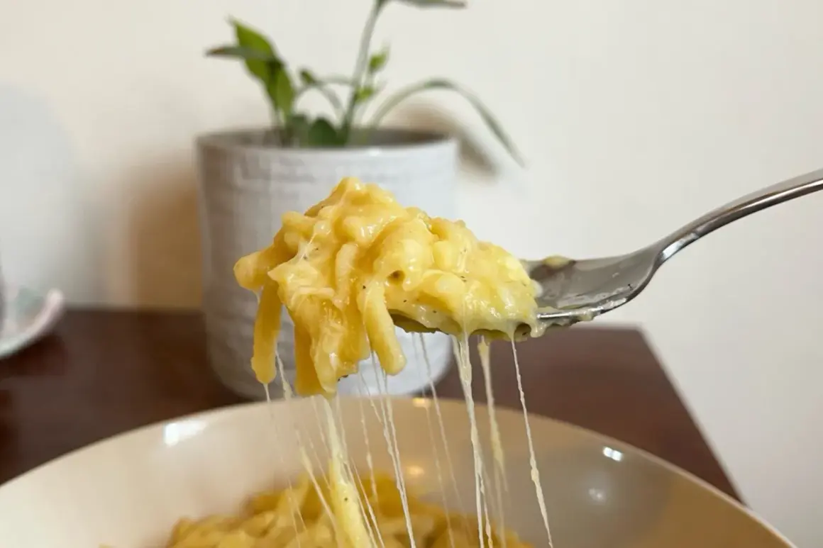 Un primo piatto cremoso: pasta e patate con provola filante, servita su una forchetta.