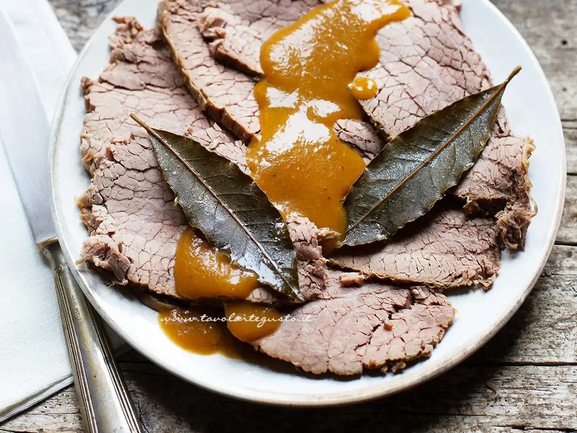 Fette di brasato di manzo succulento su un piatto, nappate con una salsa dorata e guarnite con foglie di alloro.