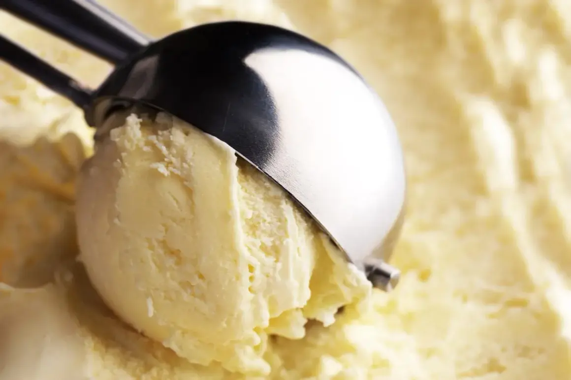 Un cucchiaio raccoglie una pallina di cremoso gelato fatto in casa, dal colore giallo pallido e dalla consistenza invitante.