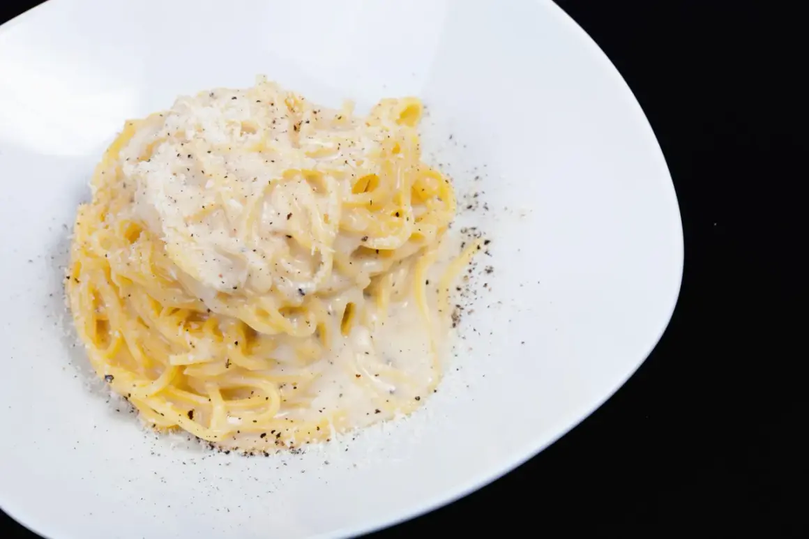 Spaghetti cremosi con formaggio e pepe nero, un classico della cacio e pepe ricetta, serviti su un piatto bianco.