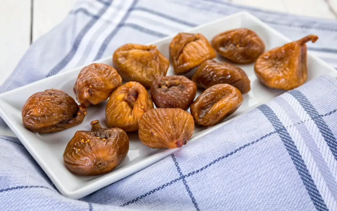 Fichi secchi al forno, caramellati e lucidi, disposti su un piatto bianco, con un tovagliolo a quadri blu e bianchi.