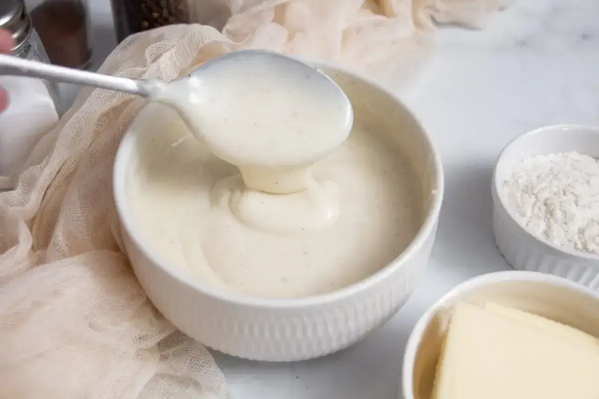 Una cucchiaiata di besciamella cremosa, pronta per la tua ricetta. Ingredienti base come farina e burro sono visibili.