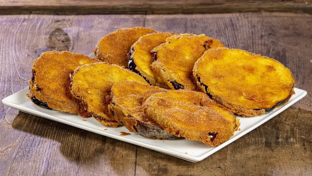 Fette dorate di melanzane fritte, impanate e croccanti, disposte su un piatto bianco.