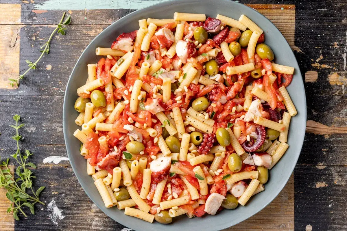 Un piatto di pasta estiva con polpo, pomodorini, olive verdi e pinoli, un'esplosione di sapori mediterranei.