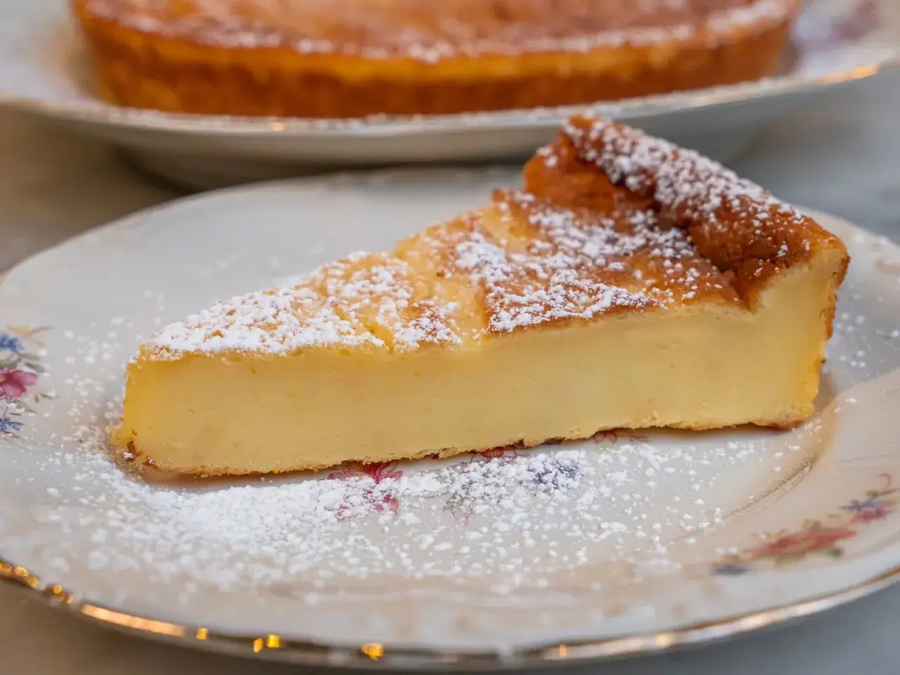 Una fetta di migliaccio napoletano ricetta della nonna, spolverata di zucchero a velo, su un piatto floreale.