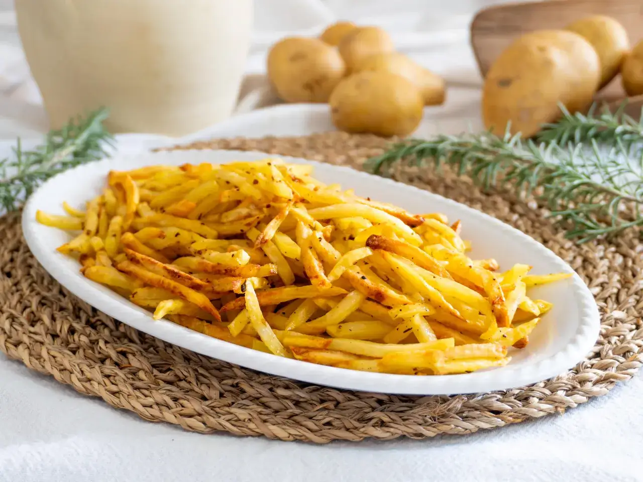 Patate in friggitrice ad aria, dorate e croccanti, servite su un piatto bianco con rosmarino.