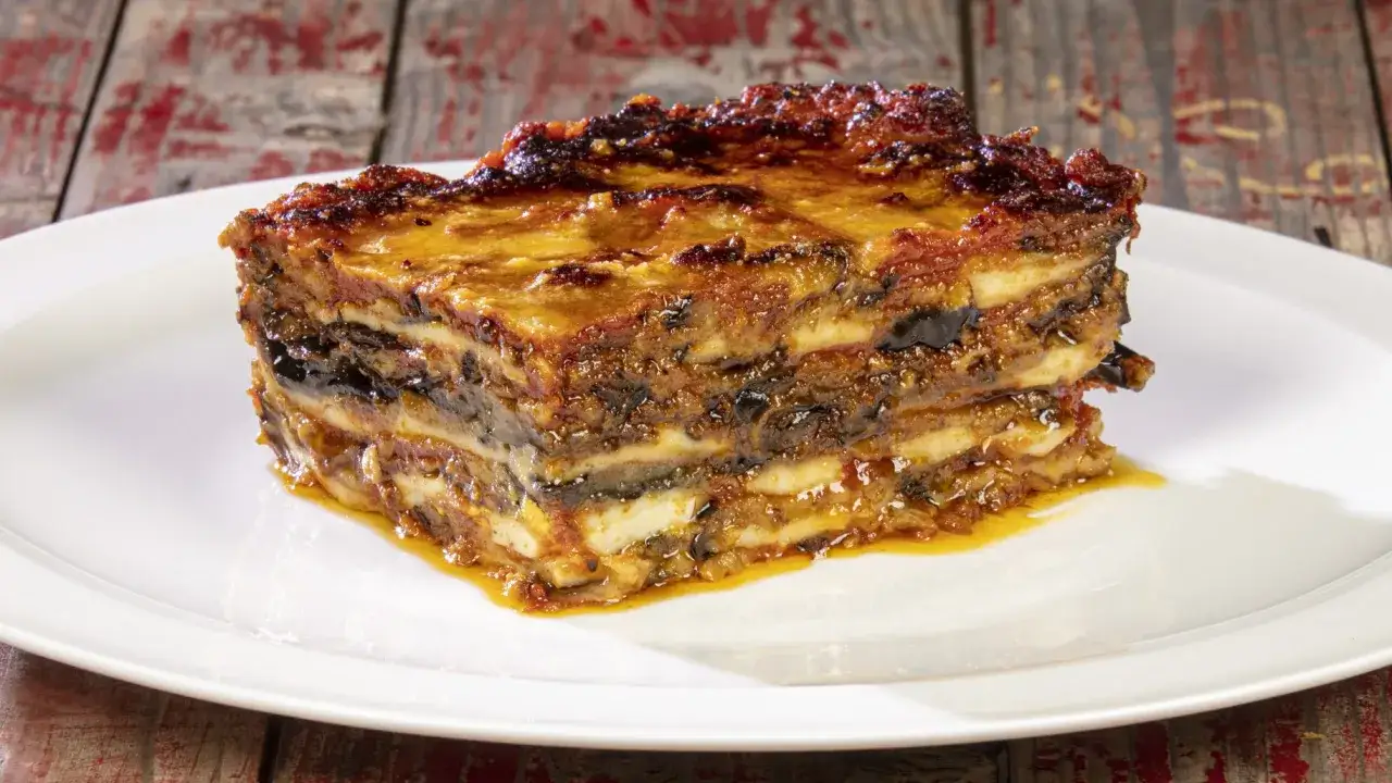 Una fetta di parmigiana di melanzane, stratificata e dorata, su un piatto bianco.
