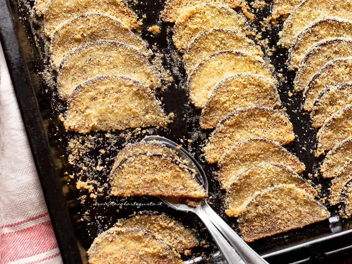 Fette di melanzane al forno, impanate e dorate, disposte su una teglia. Un piatto gustoso e leggero.