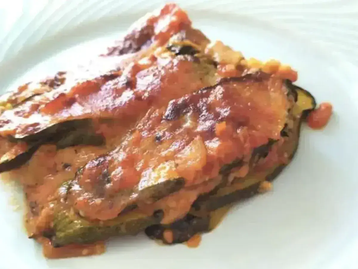 Una fetta di parmigiana di zucchine light, con strati di verdura e sugo di pomodoro, servita su un piatto bianco.