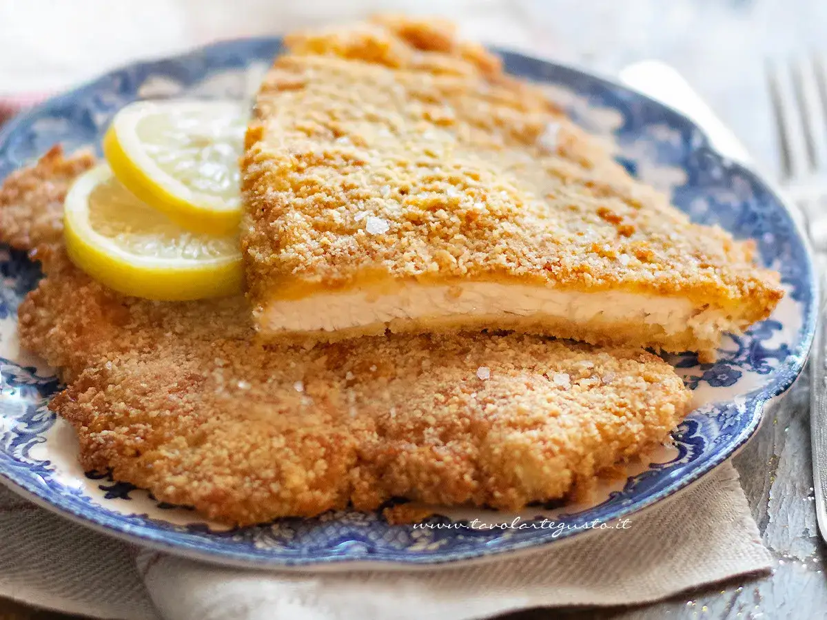 Deliziose cotolette di pollo al forno, dorate e croccanti, servite su un piatto blu con spicchi di limone.