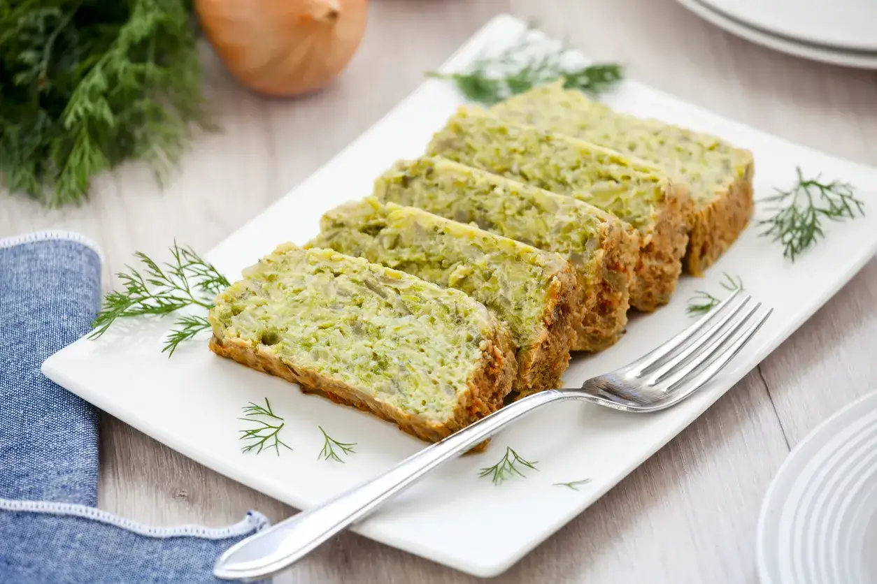 Sformato di zucchine affettato su un piatto bianco, guarnito con aneto. Un contorno leggero e saporito.