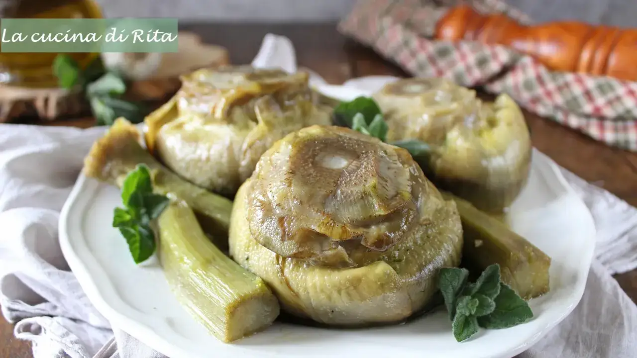 Carciofi alla romana cotti a puntino, teneri e profumati, serviti su un piatto bianco con rametti di menta.