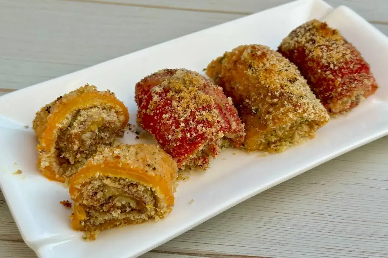 Peperoni ripieni al forno, dorati e croccanti, serviti su un piatto bianco. Un antipasto invitante e gustoso.