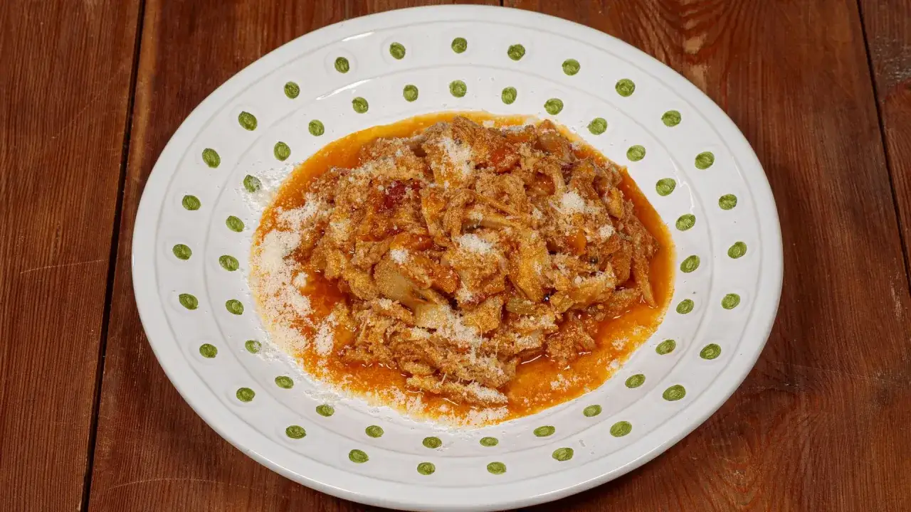 Un piatto di trippa alla fiorentina, ricca e saporita, cosparsa di parmigiano grattugiato, servita su un piatto bianco decorato.