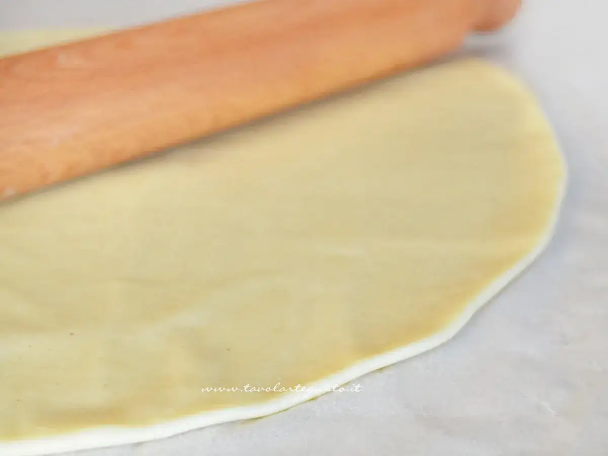 Mattarello stende la pasta brise su carta forno, pronta per una deliziosa torta salata.